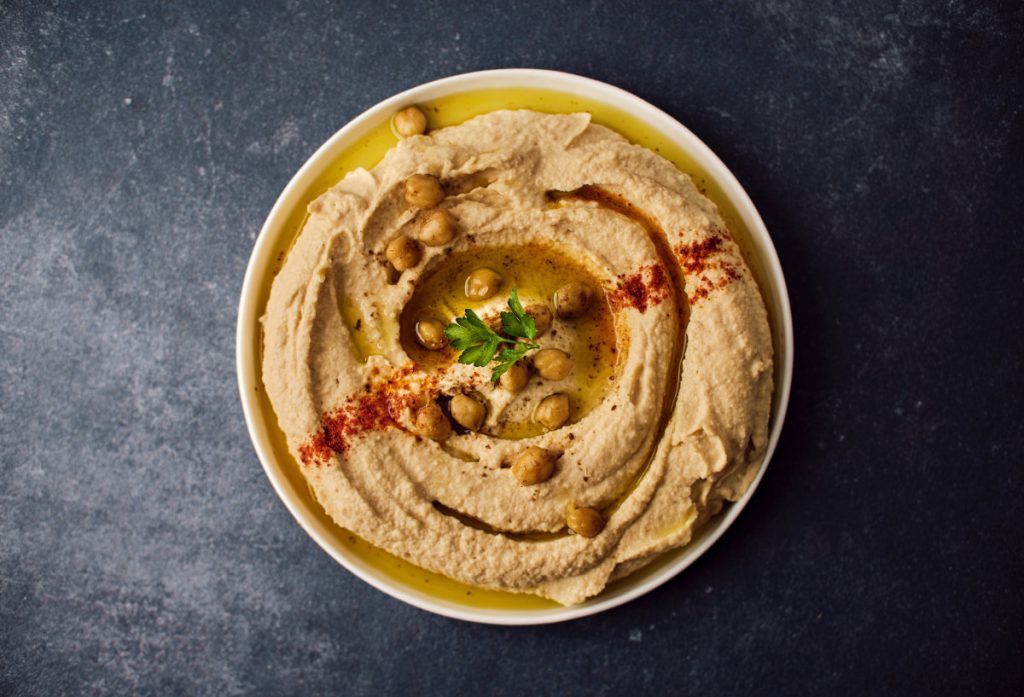 A hummus dip in a bowl garnished with chick peas, paprika, and cilantro.