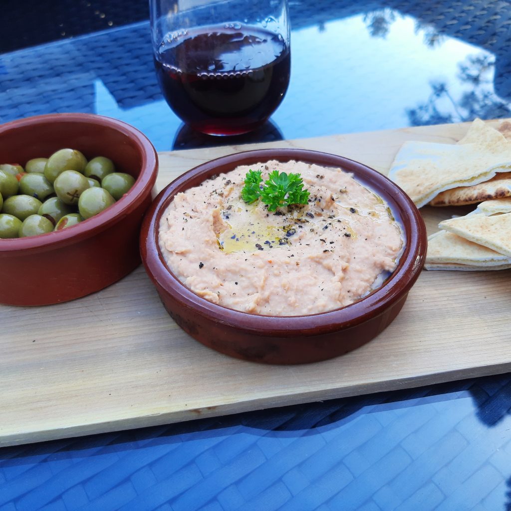 A bowl of hummus with a side of pita and olives